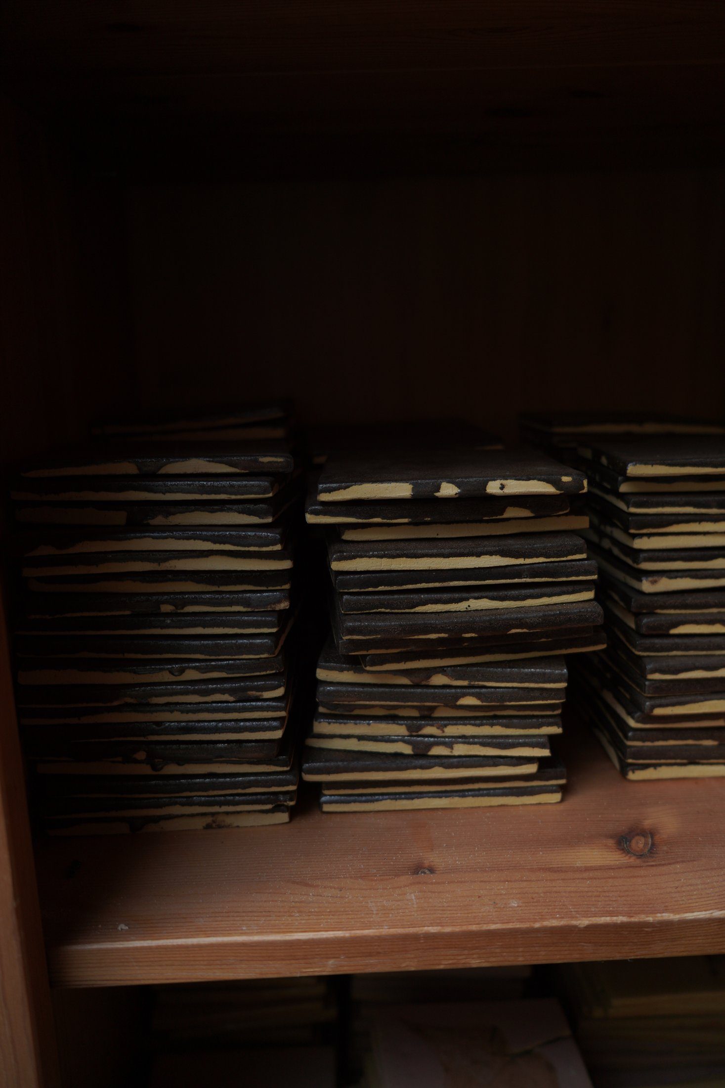 Dark finished handmade tile stacks held on wooden shelving.