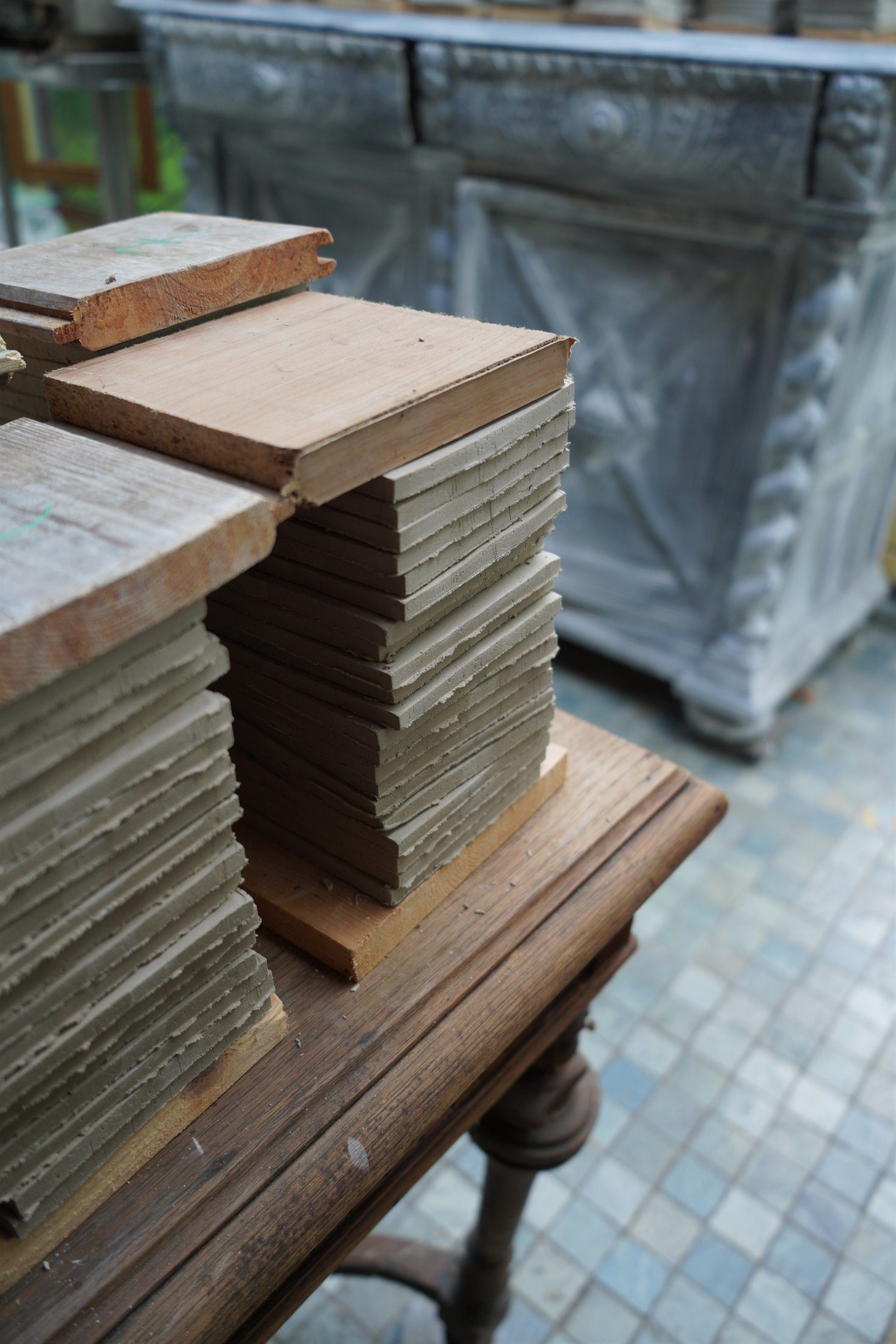 Raw handmade tile stacks settling under wooden boards in the atelier.