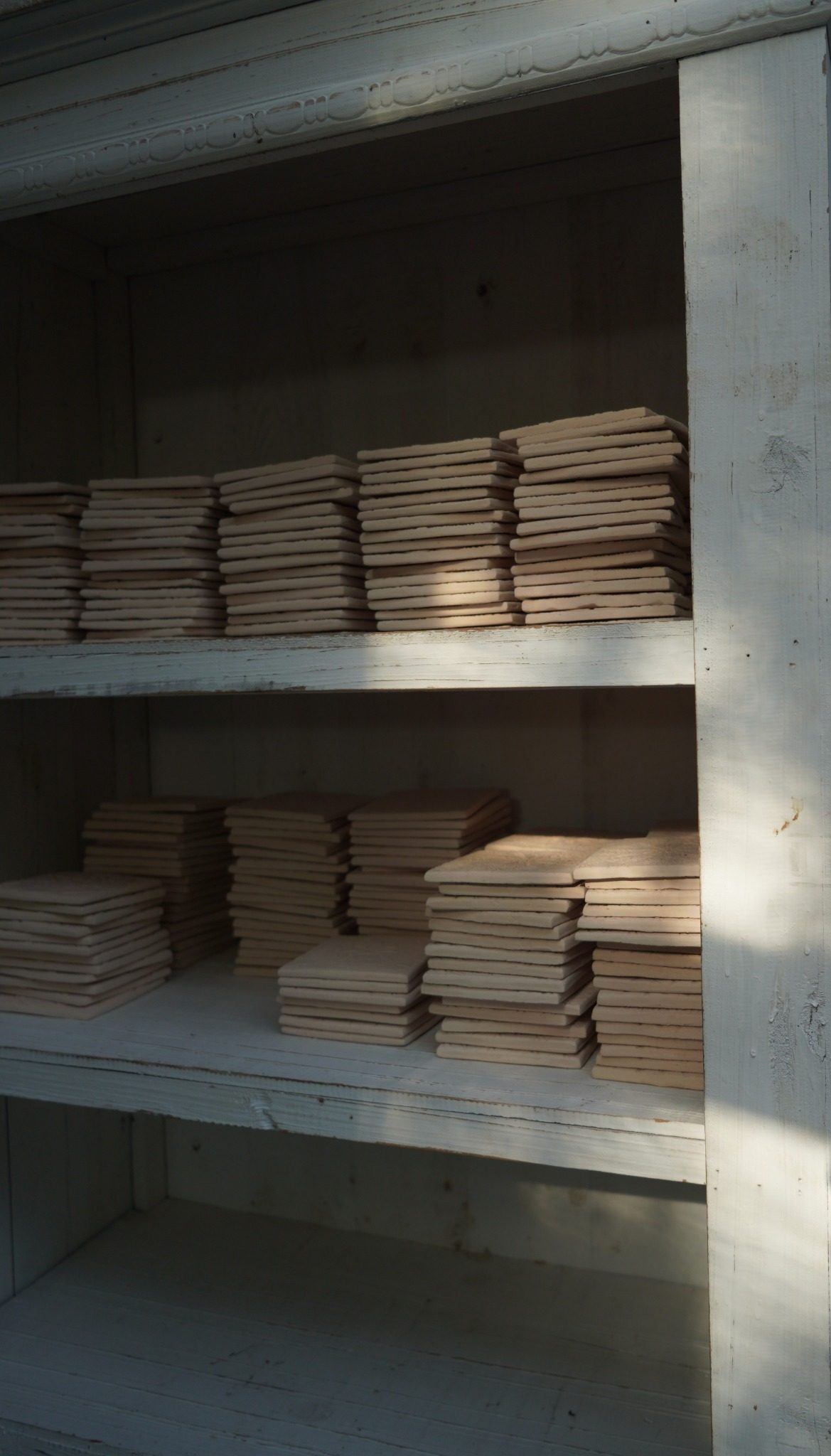 Bisque-fired tile stacks held in the atelier for finishing.