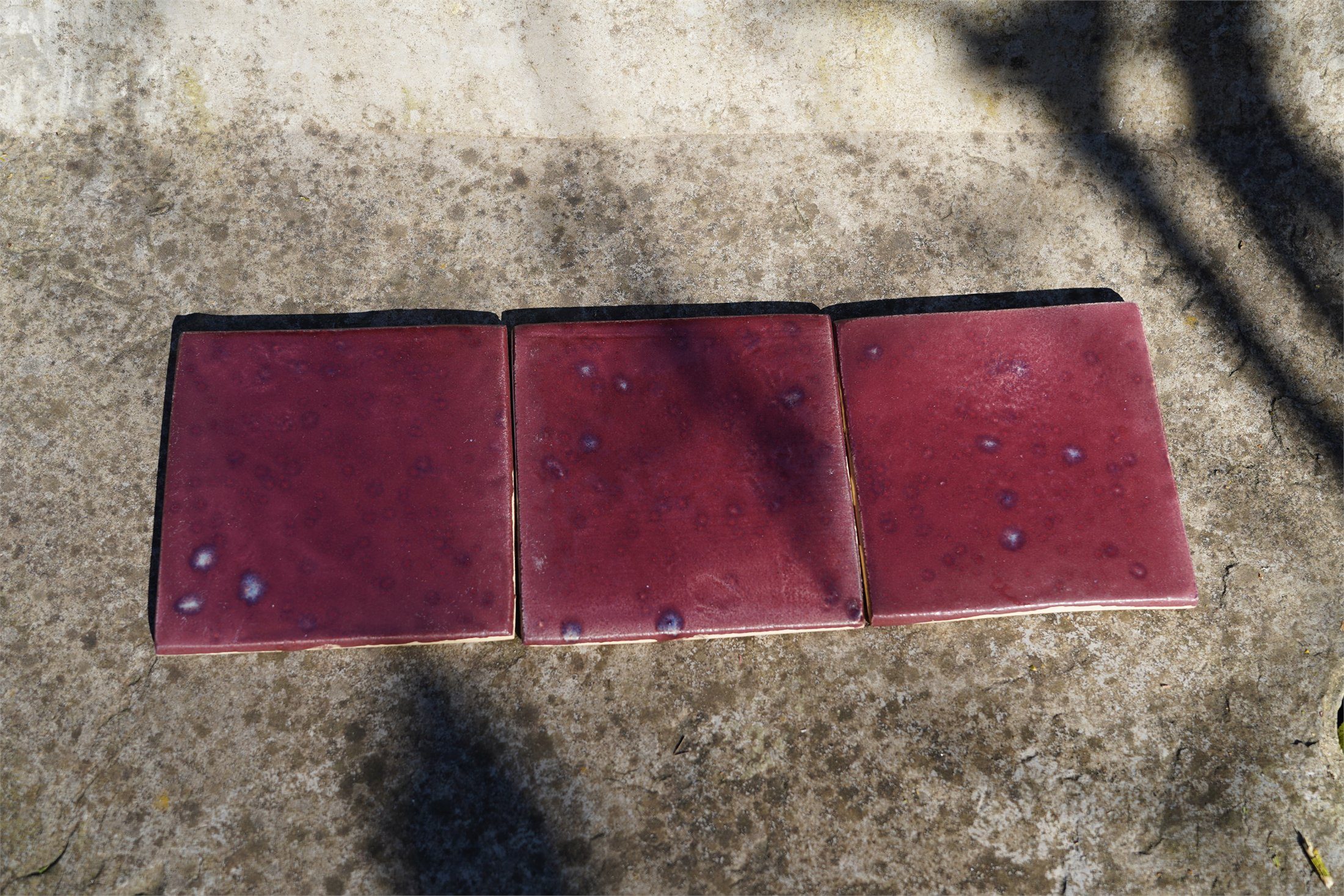 Three burgundy handmade tiles on Belgian stone showing related but distinct glaze movement.