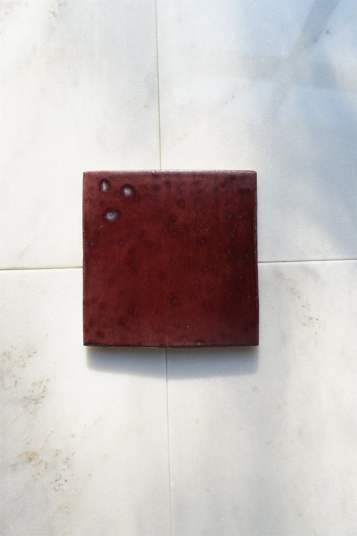 Burgundy glaze on handmade ceramic tile, photographed on Carrara marble.