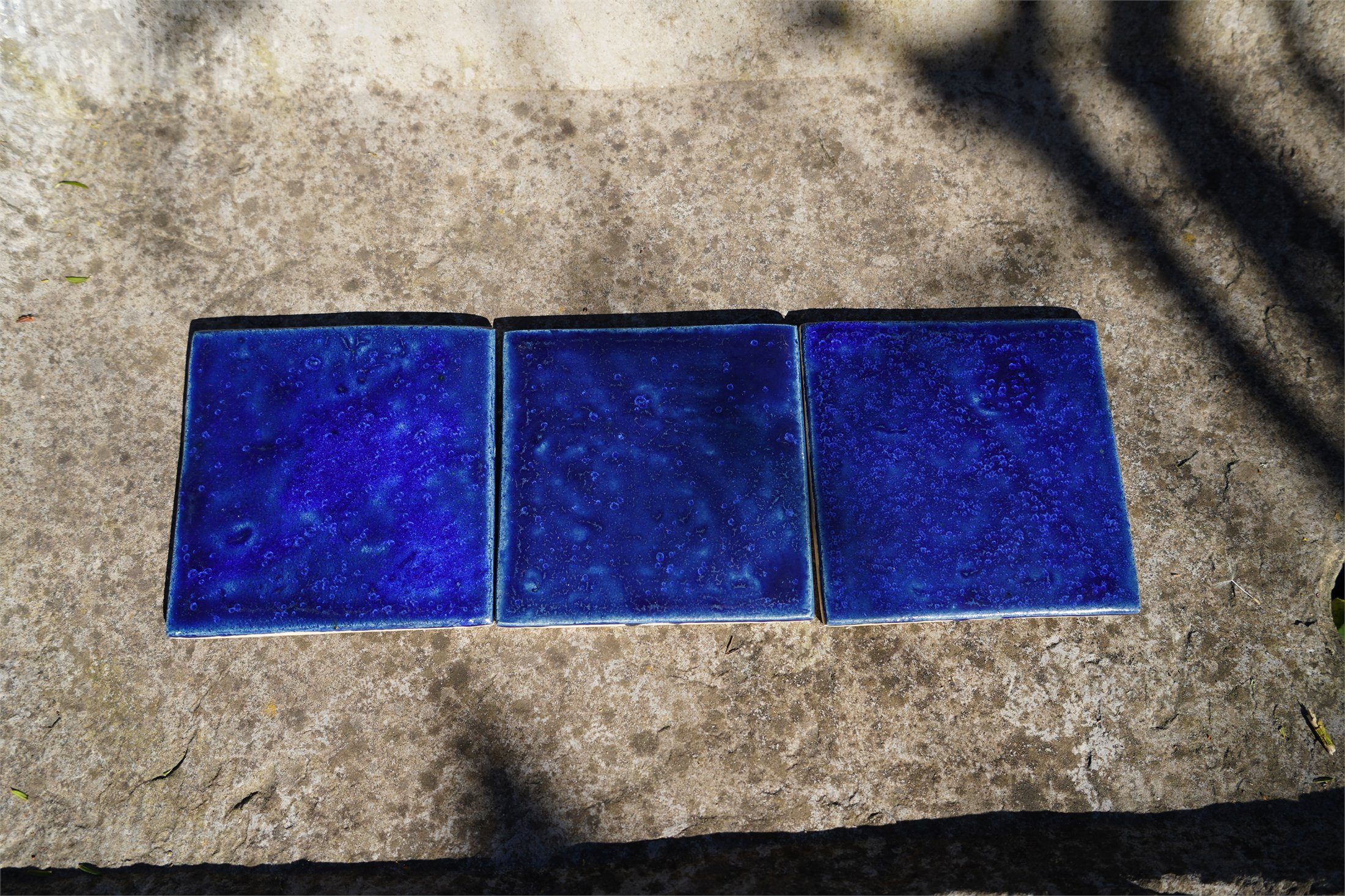 Three cobalt handmade tiles on Belgian stone showing natural batch variation.