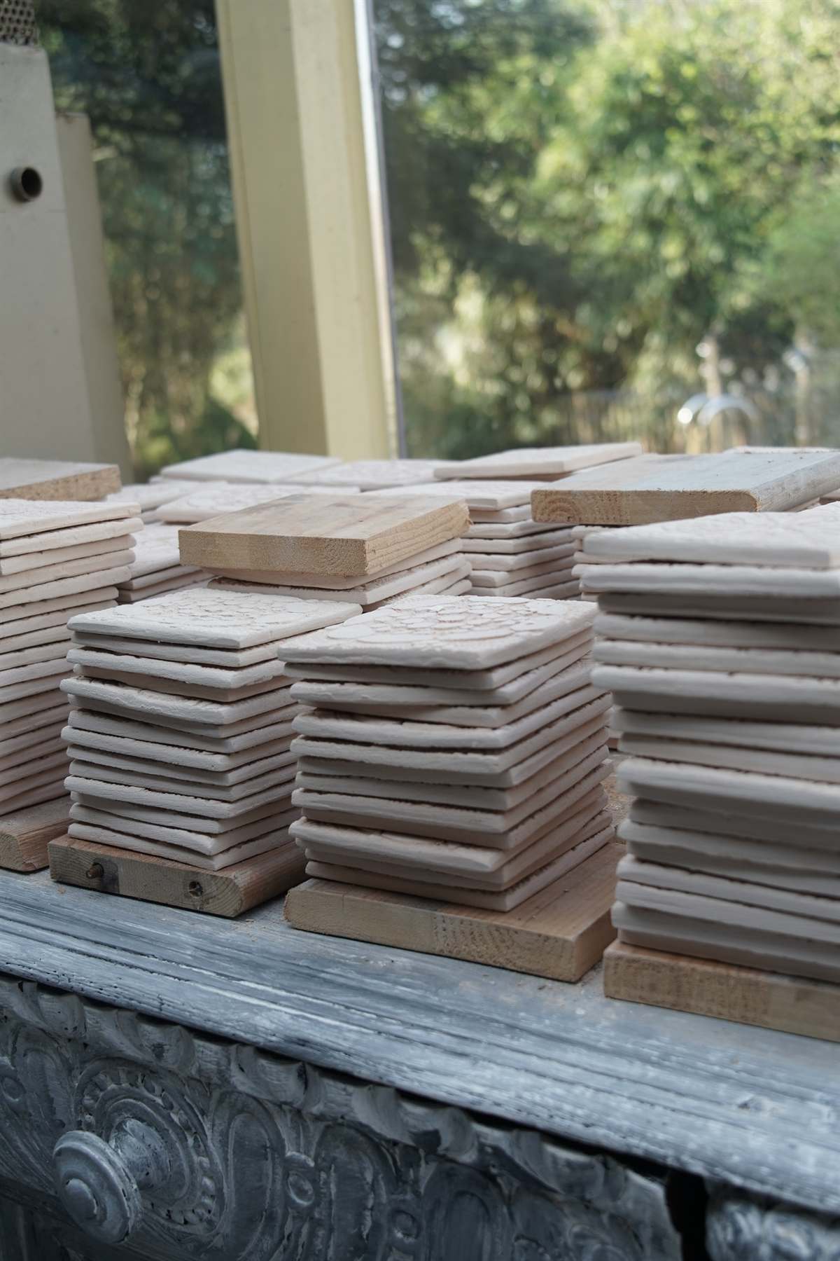 Sunlit raw tile stacks drying between pieces of wood.
