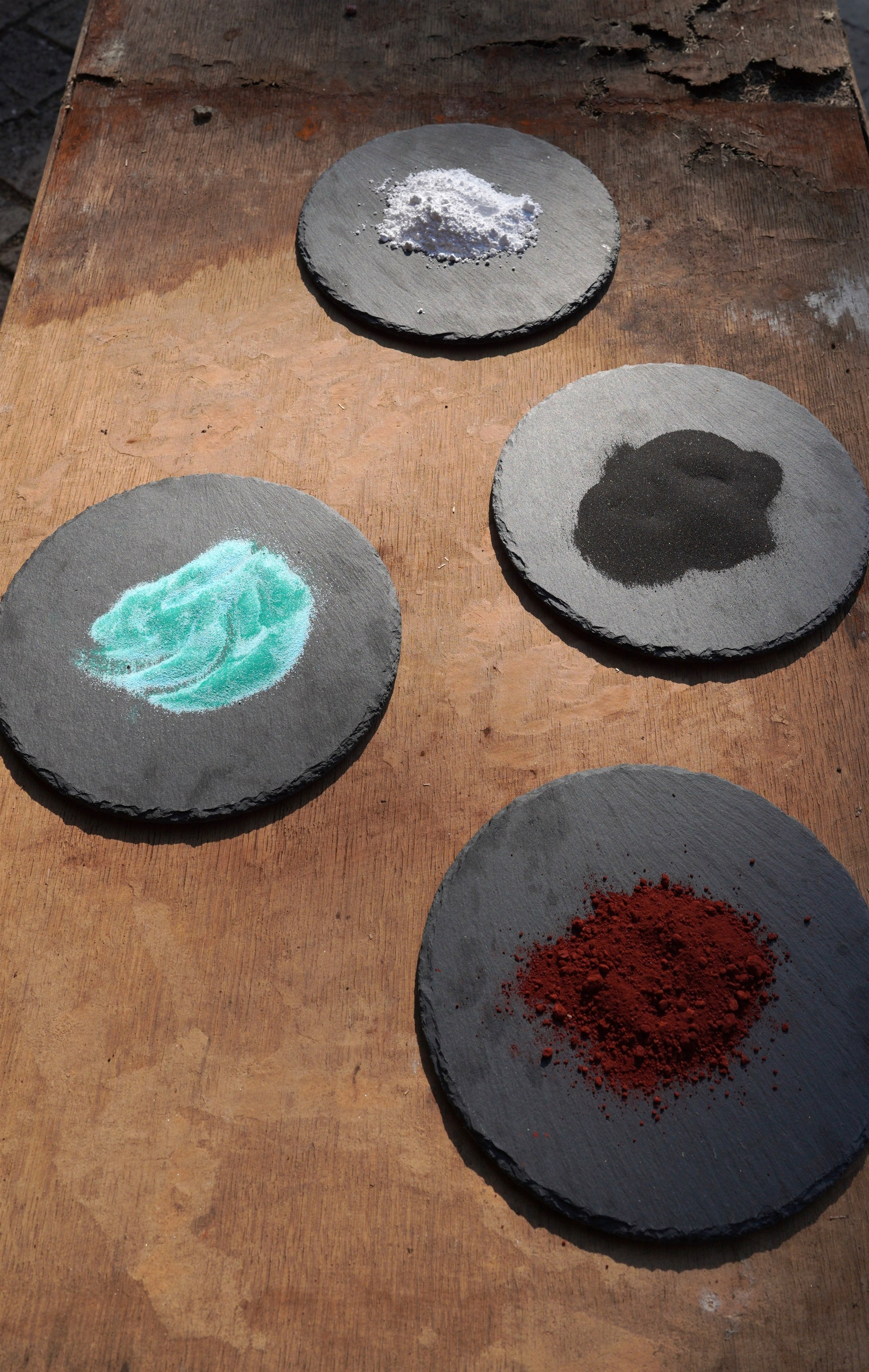 Ceramic pigment powders arranged on slate palettes in the atelier.