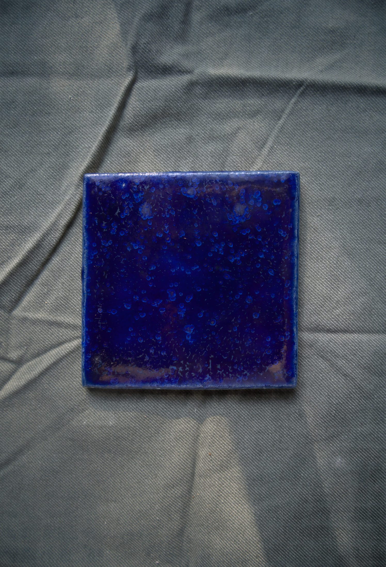 Single sapphire blue tile on woven cloth.