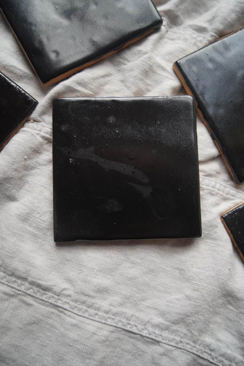 Single black handmade tile on pale cloth.