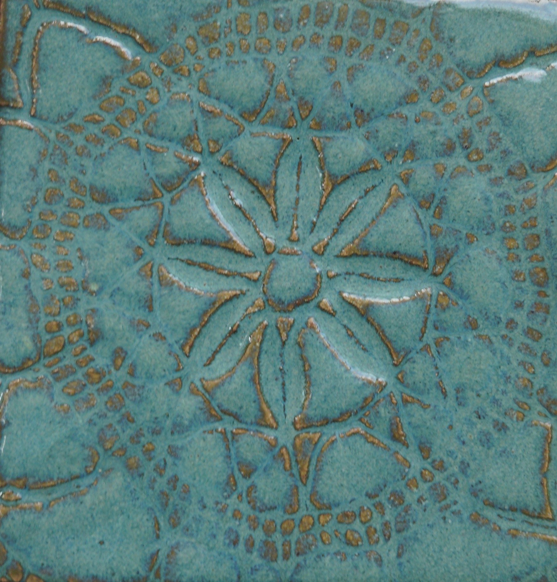 Close-up of verdigris relief tile showing glaze pooling and lace-inspired pattern.